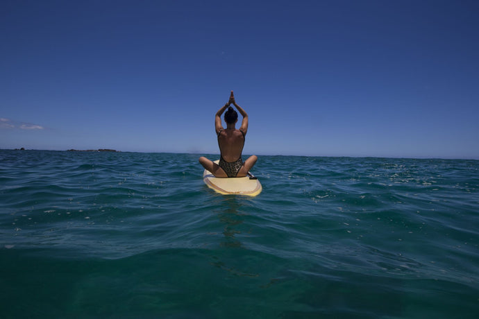 Rear view of woman sitting on paddleboard doing yoga, Hawaii, USA